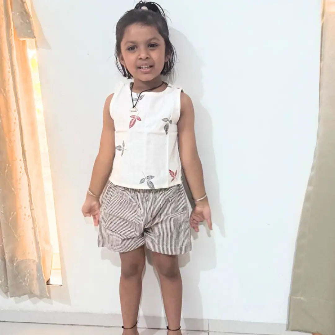 Young girl wearing a white sleeveless top with floral patterns and checkered shorts indoors