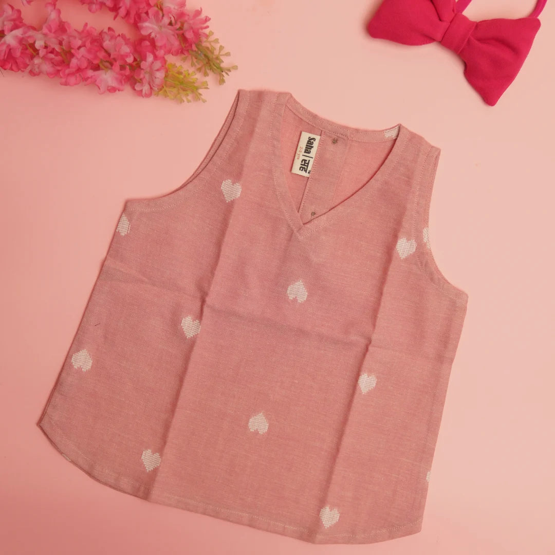 Flat lay of sleeveless pink handloom cotton top with white heart motifs and soft minimalist detailing for girls
