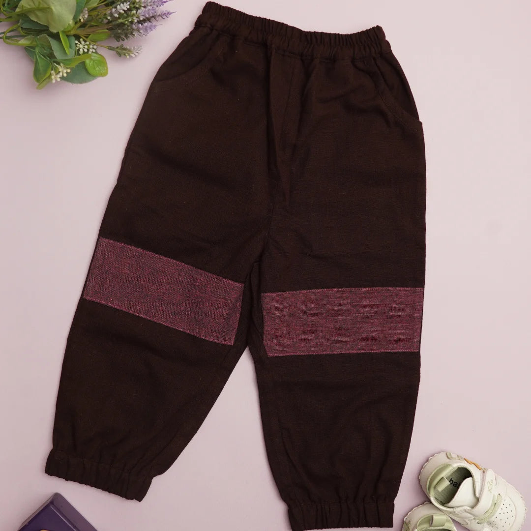 Flat lay of dark cotton joggers with contrasting knee patches, elastic waistband, and cuffed hems.