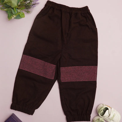 Flat lay of dark cotton joggers with contrasting knee patches, elastic waistband, and cuffed hems.