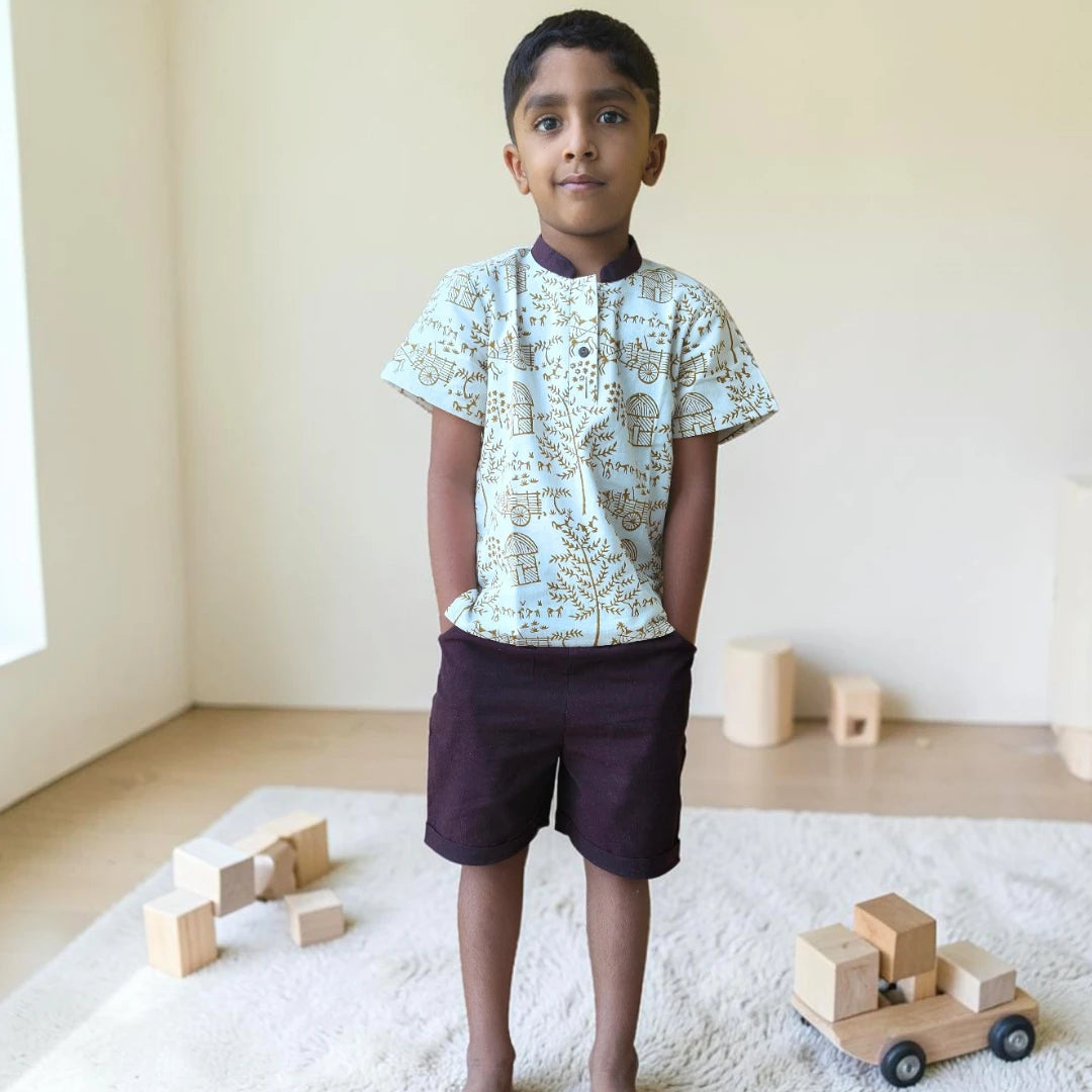 Young boy wearing a handblock-printed khadi short kurta set with dark Ikat shorts, standing indoors with wooden toys and minimalist decor.