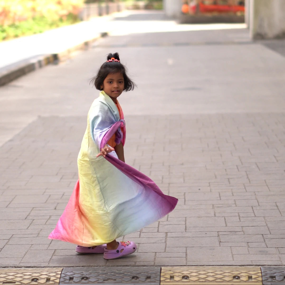 Child wearing a soft rainbow semi-giant playsilk as a flowing cape during imaginative outdoor play.
