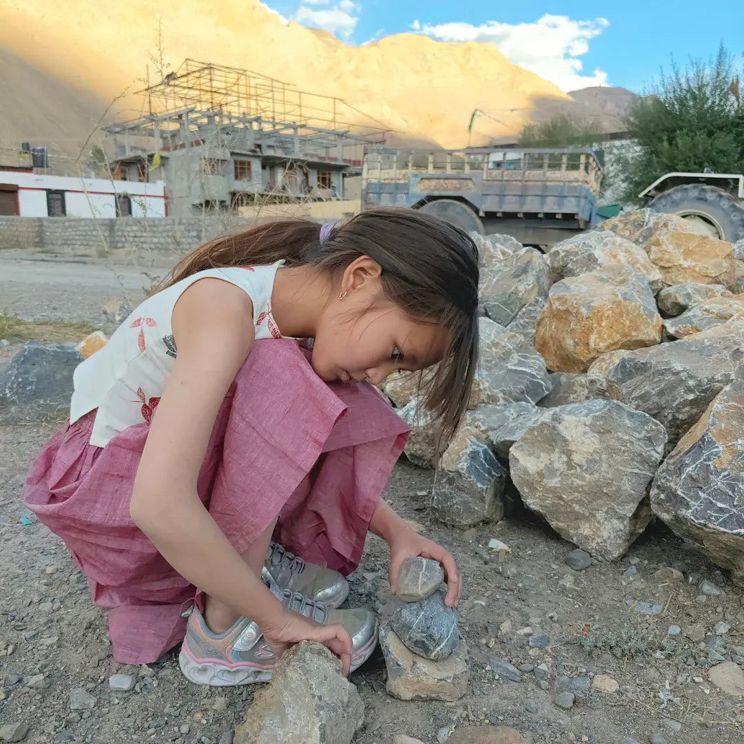 Child playing with rocks in a mountainous area with construction in the background