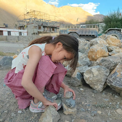 Child playing with rocks in a mountainous area with construction in the background