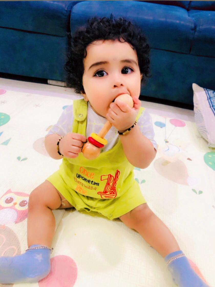 Baby playing with wooden rattle sitting on a colorful play mat 