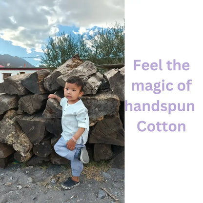 Toddler in light purple handspun cotton joggers playing by a woodpile outdoors