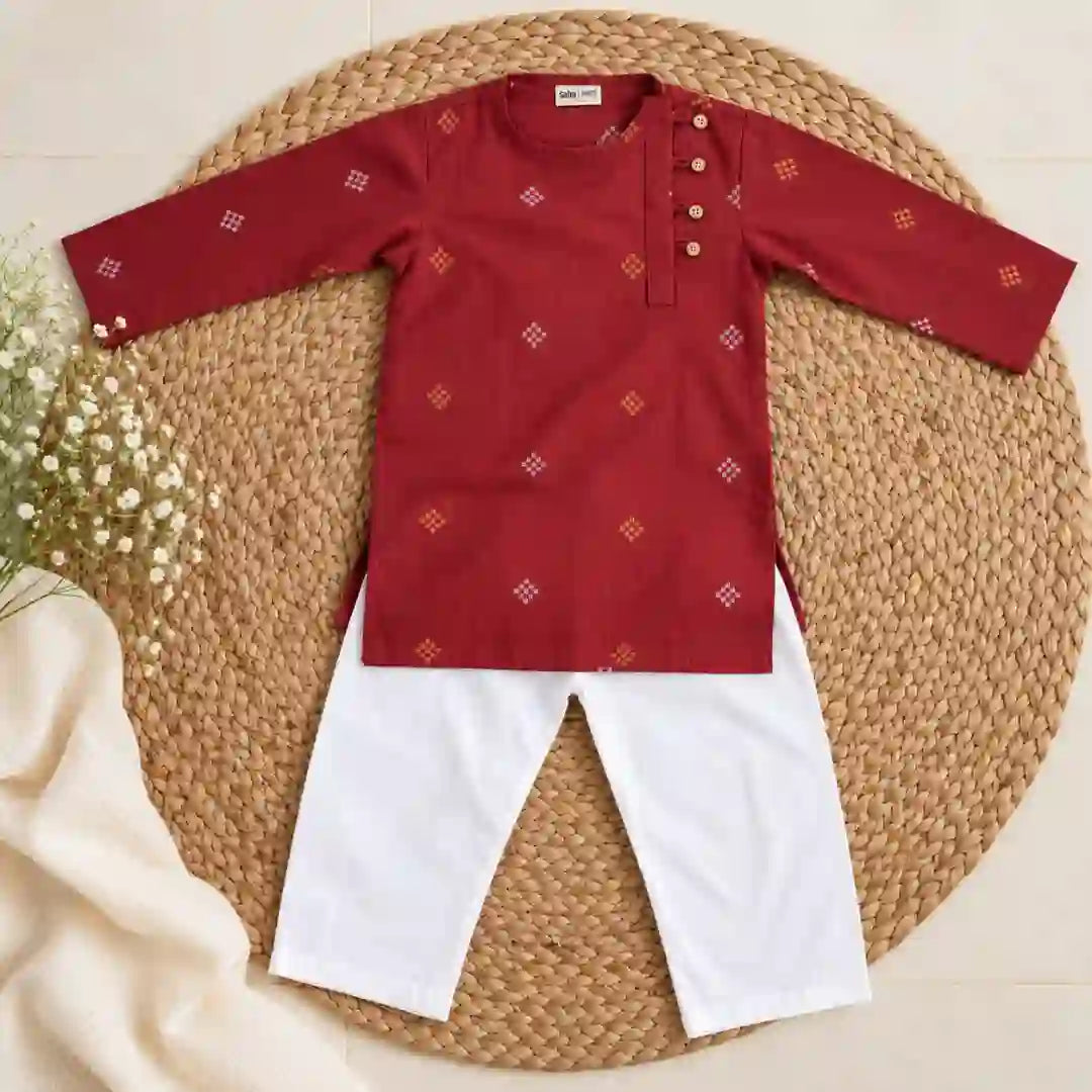 Flat lay of a maroon full sleeve kurta with gold and white motifs and four buttons beside a white pajama