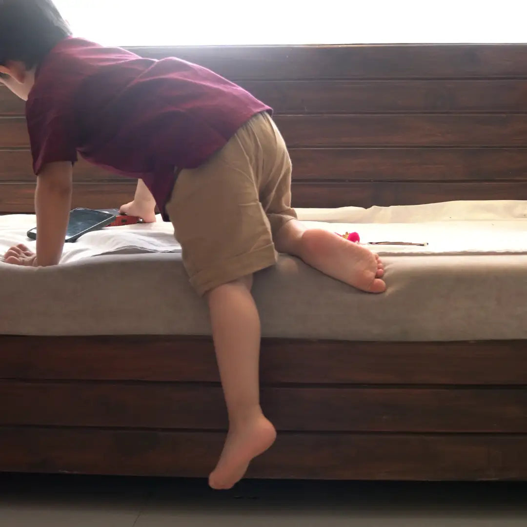 Boy climbing onto a bed in a maroon shirt and beige shorts, moving freely