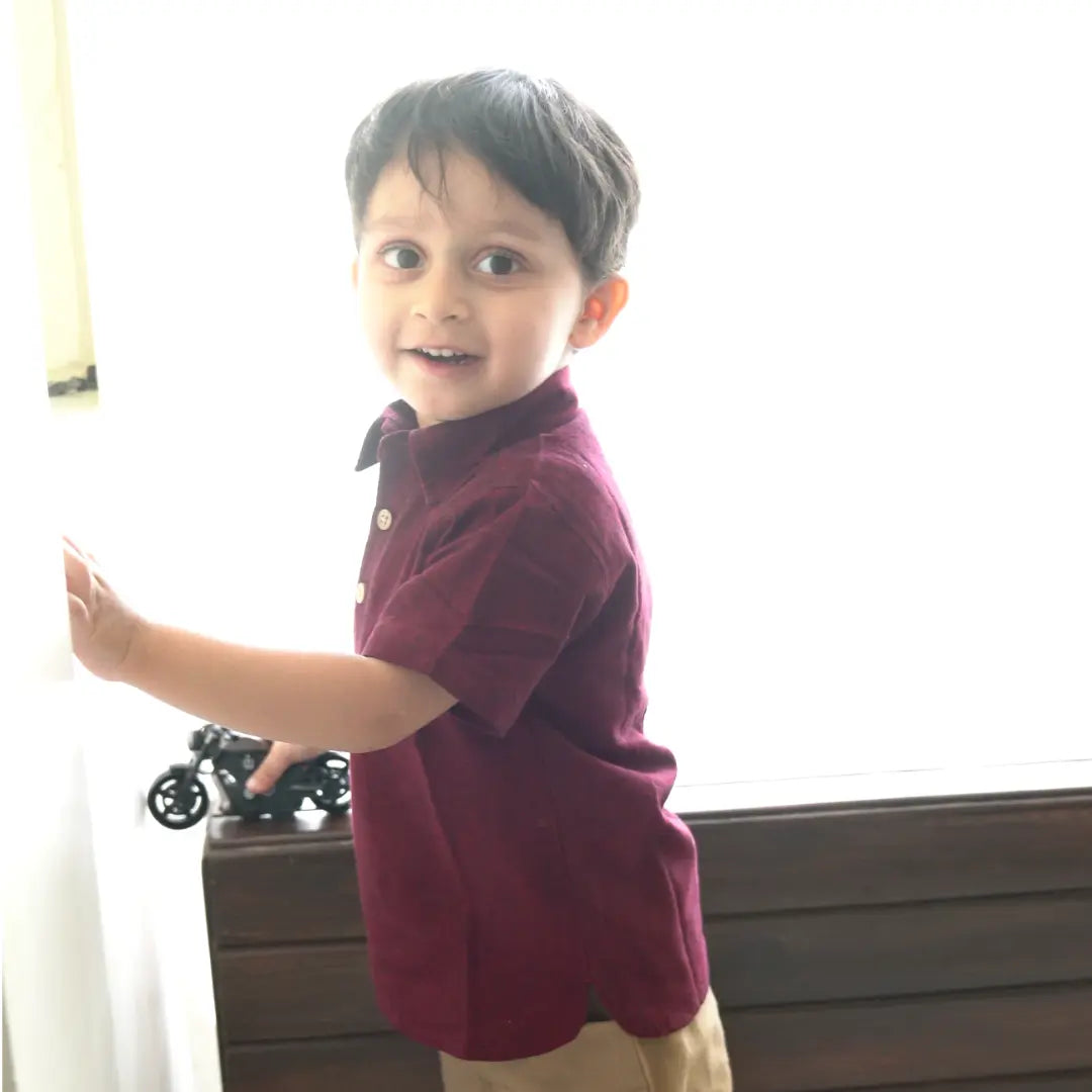 Smiling boy in a maroon handwoven ikkat polo neck shirt standing by a window