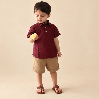 Toddler in a maroon handwoven ikkat polo neck shirt and beige cuffed shorts holding a small toy