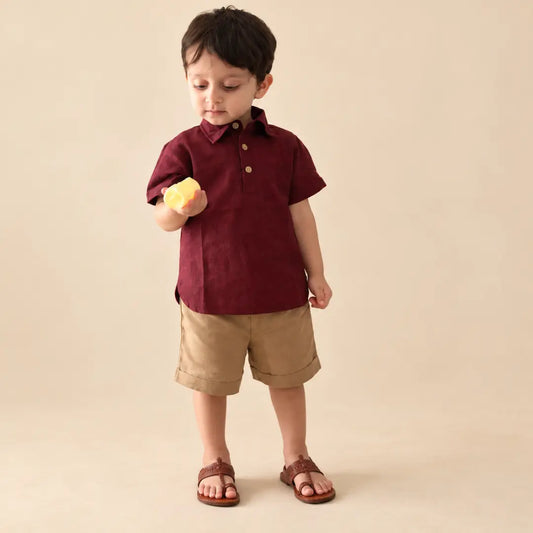 Toddler in a maroon handwoven ikkat polo neck shirt and beige cuffed shorts holding a small toy