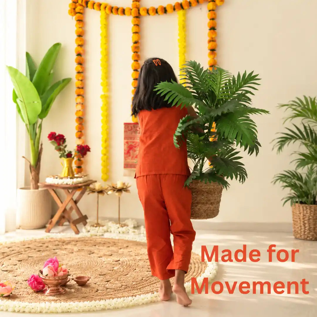 Girl in a rust orange ikat coord set carrying a potted plant past festive marigold garlands, made for movement
