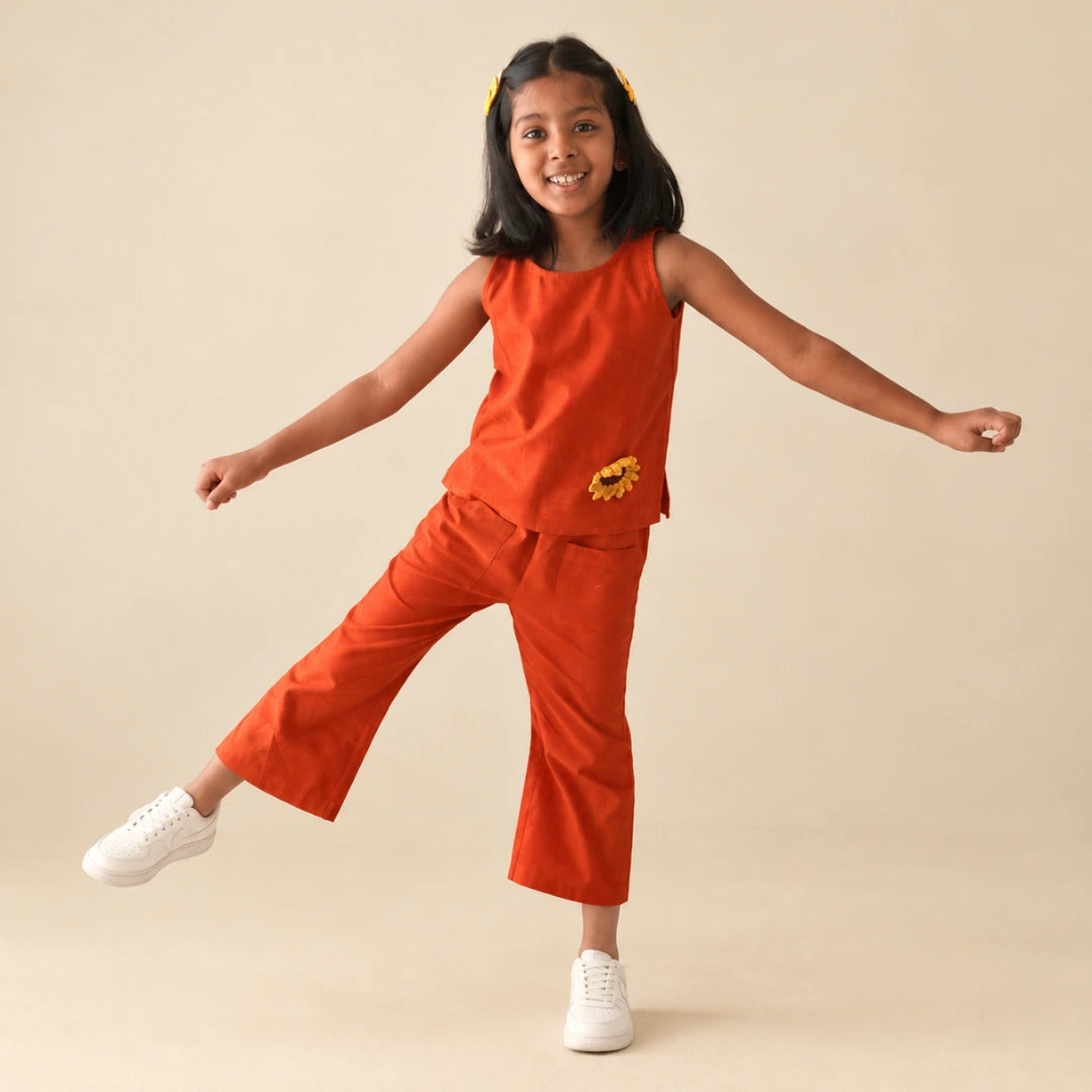 Girl in a rust orange handwoven ikat coord set with a crochet sunflower, balancing playfully on one leg