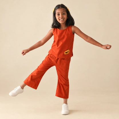 Girl in a rust orange handwoven ikat coord set with a crochet sunflower, balancing playfully on one leg