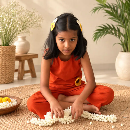 Girl in a rust orange ikat coord set sitting cross-legged on a jute mat, arranging jasmine flowers