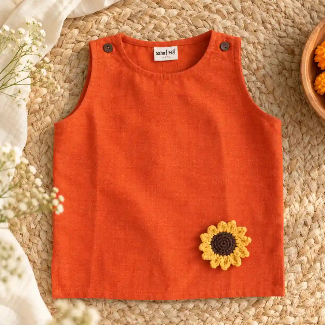 Rust orange sleeveless ikat top with shoulder buttons and a hand-crocheted sunflower in cotton yarn