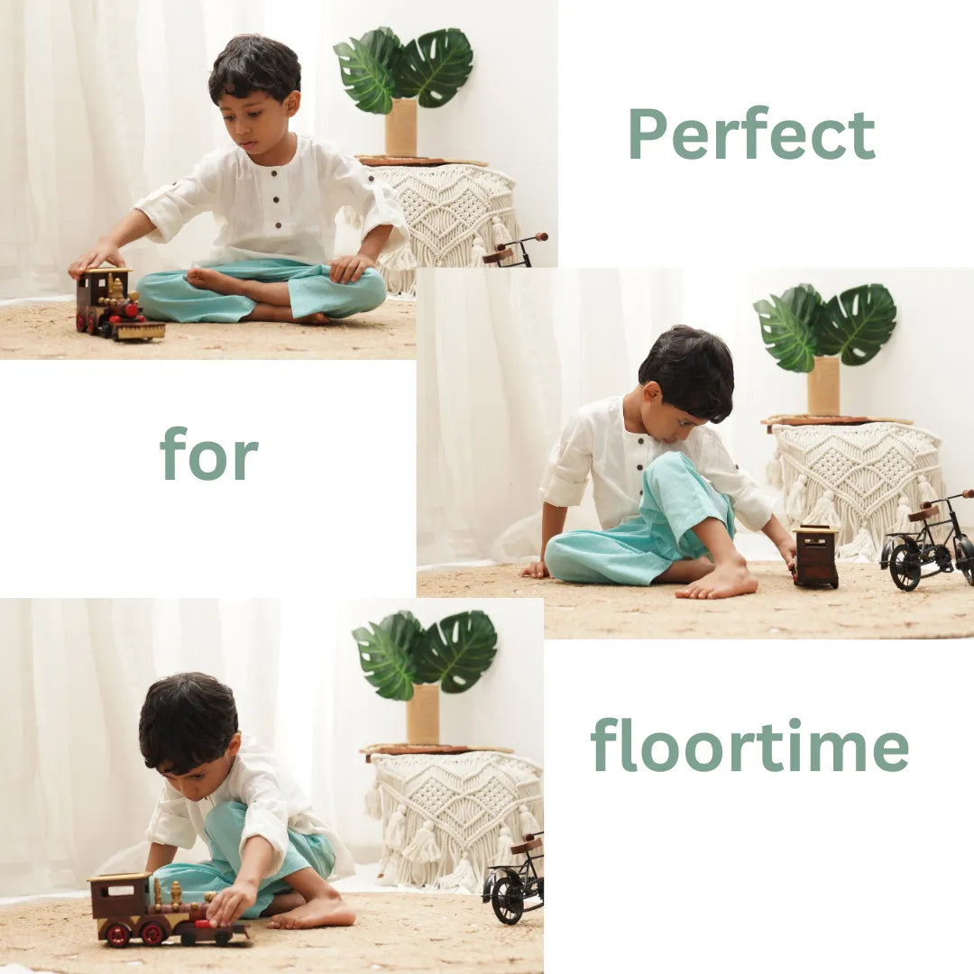 Child sitting cross-legged in teal blue cotton pants playing with a wooden train during floortime