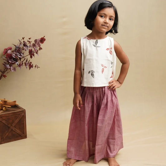 Young girl wearing a floral top and pink pants standing against a beige background